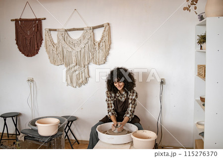 Young female potter working on pottery wheel in cozy studio Young female potter working on pottery wheel in cozy studio 115276370