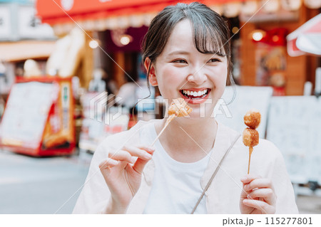 大阪 新世界で名物の串カツを食べる若い女性 115277801