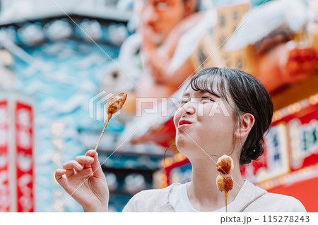 大阪 新世界で名物の串カツを食べる若い女性 115278243