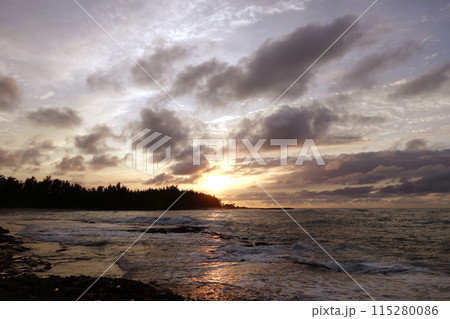 Sunset through the clouds and over the trees as it reflects on the watery waves at Kawela Bay rocky shore Sunset through the clouds and over the trees as it reflects on the watery waves at Kawela Bay rocky shore 115280086