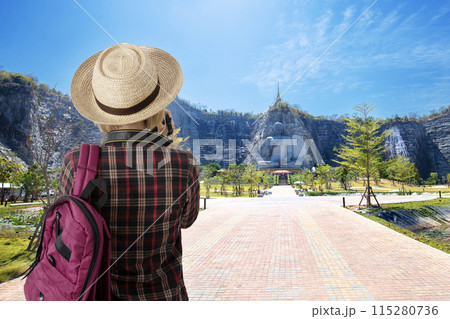 Female tourist enjoy taking photo of beautiful big stone buddha on the hill. Female tourist enjoy taking photo of beautiful big stone buddha on the hill. 115280736