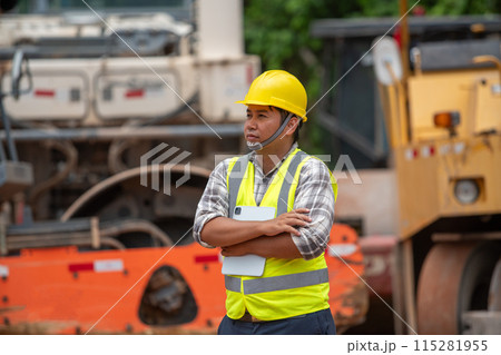 The engineer supervising the construction of the asphalt road stood with his arms crossed 115281955