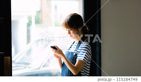 スマホを見る女性カフェ店員 スマホを見る女性カフェ店員 115284749
