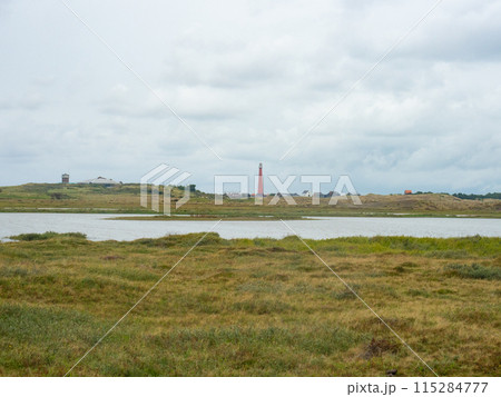 Den Helder, Netherlands - August 6th 2023: Coastal landscape with lakes and the red lighthouse Den Helder, Netherlands - August 6th 2023: Coastal landscape with lakes and the red lighthouse 115284777
