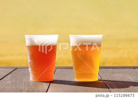 テーブルの上に2種類のビールが置かれている。プラスチックコップを使用。麦畑の背景 テーブルの上に2種類のビールが置かれている。プラスチックコップを使用。麦畑の背景 115286673