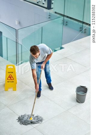 Man, janitor and mopping office floor or cleaning hygiene with caution sign or water, soap or bacteria. Male person, disinfection and corporate building as washing service or dirty, wellness or job 115288302