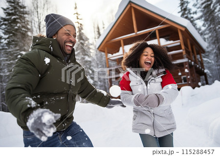 Joyful couple having energy snowball fight outside winter holiday log cabin 115288457