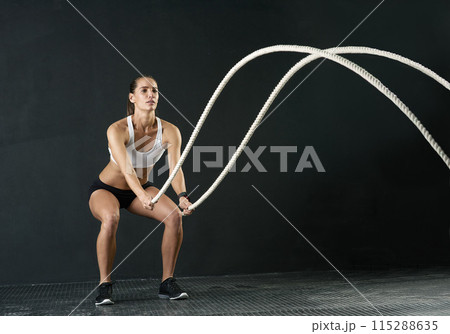 Woman, studio and training with battle rope for fitness, calorie and body workout for vitality or wellness. Girl, squat and exercise on black background for strength, power and endurance or gym 115288635