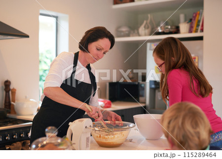 Mother, children and baking in kitchen in home, family and bonding together with mixing machine on counter table. Mom, apron and daughter with son watching, waiting for cookie dough in apartment 115289464
