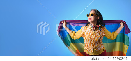 Elegant senior lady holding rainbow flag on blue background. LGBT, human rights, freedom and equality concept 115290241