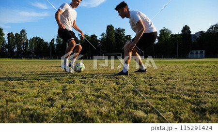 Two sportsmen playing in soccer in stadium at sunset. Professional footballers performing tricks with ball at green field. Young men training at meadow. Concept of a freestyle football. Slow motion Two sportsmen playing in soccer in stadium at sunset. Professional footballers performing tricks with ball at green field. Young men training at meadow. Concept of a freestyle football. Slow motion 115291424