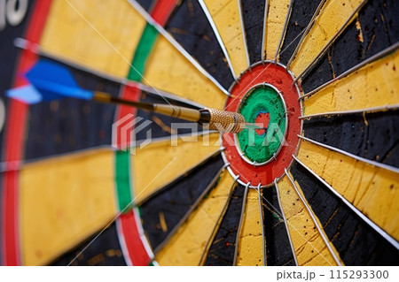 A dartboard with a single dart perfectly placed in the bullseye. 115293300