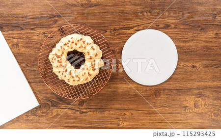 Flat lay. Carefully placing the gingerbread bundt cake, adorned with salted caramel frosting and gingerbread sprinkles, into a white paper bundt cake box with a clear window for gifting. 115293425