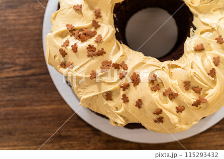Carefully placing the gingerbread bundt cake, adorned with salted caramel frosting and gingerbread sprinkles, into a white paper bundt cake box with a clear window for gifting. 115293432