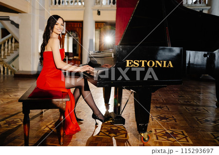 A luxurious actress in a red dress plays the piano in the great hall of the theater A luxurious actress in a red dress plays the piano in the great hall of the theater 115293697