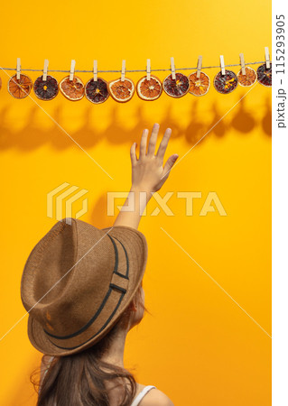 Girl reaches for dried orange slices hanging on a rope. Girl reaches for dried orange slices hanging on a rope. 115293905