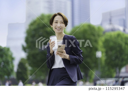 タンブラーとスマホを手に持つビジネスウーマン 115295347