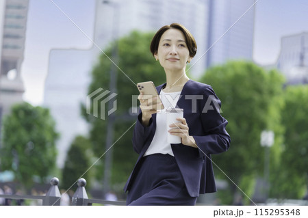 タンブラーとスマホを手に持つビジネスウーマン 115295348