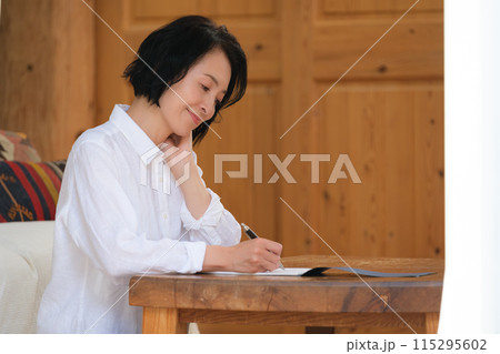リビングで家族への手紙を書くミドル女性 115295602