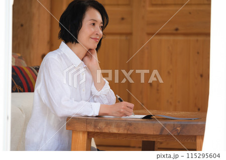 リビングで家族への手紙を書くミドル女性 リビングで家族への手紙を書くミドル女性 115295604