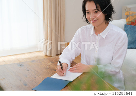 リビングで家族への手紙を書くミドル女性 リビングで家族への手紙を書くミドル女性 115295641