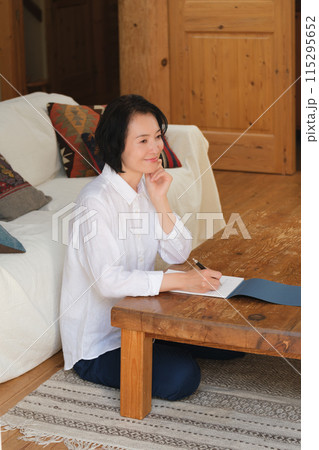 リビングで家族への手紙を書くミドル女性 リビングで家族への手紙を書くミドル女性 115295652