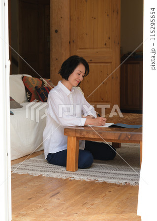 リビングで家族への手紙を書くミドル女性 リビングで家族への手紙を書くミドル女性 115295654