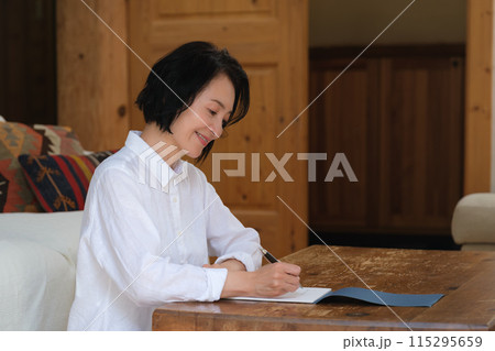 リビングで家族への手紙を書くミドル女性 リビングで家族への手紙を書くミドル女性 115295659