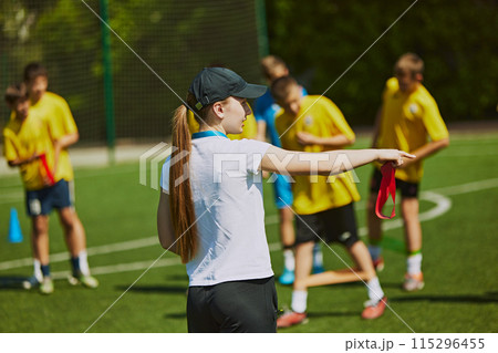 Group of young athletes, children training football outdoors with female coach on warm sunny day. Hobby and teamwork. 115296455