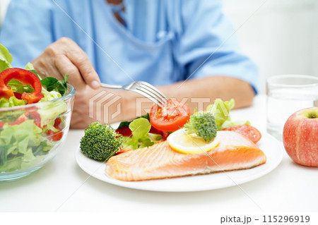 Asian elderly woman patient eating salmon stake and vegetable salad for healthy food in hospital. Asian elderly woman patient eating salmon stake and vegetable salad for healthy food in hospital. 115296919