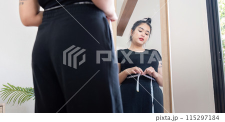 Young woman measuring waist in front of mirror. Concept of fitness and body positivity 115297184