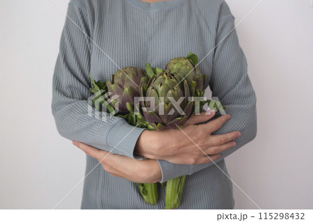 Hands gently holding fresh artichokes, showcasing nature's green bounty with care 115298432