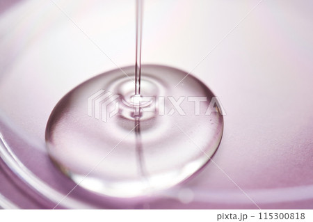 Serum or cosmetic oil flows into a transparent bowl on a purple background. 115300818