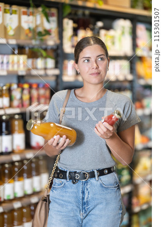 Female customer comparing two bottles of juice in grocery store 115301507