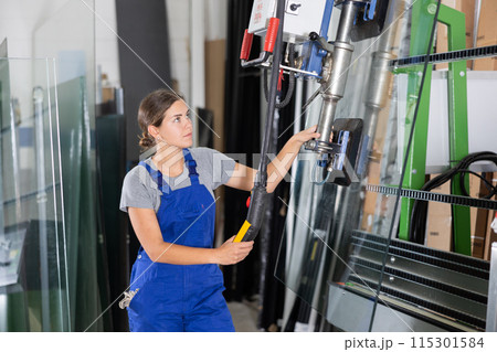 Female worker using control panel and lifting mechanism controls movement of window panes in an industrial workshop Female worker using control panel and lifting mechanism controls movement of window panes in an industrial workshop 115301584