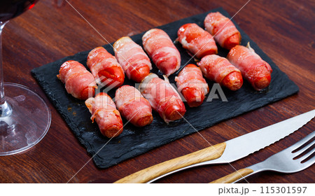 Rolled bacon with sausages on black dish 115301597