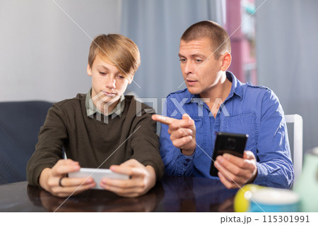 Father and son together playing on their smartphones while sitting at table at home 115301991