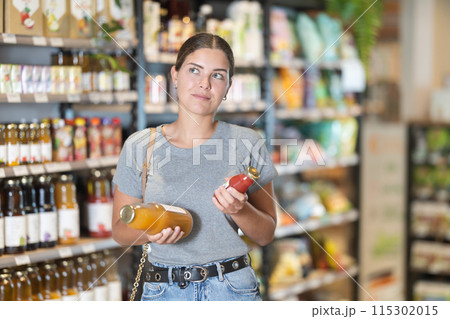 Female customer comparing two bottles of juice in grocery store 115302015
