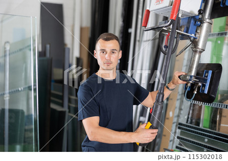 Male worker using control panel and lifting mechanism controls movement of window panes in an industrial workshop Male worker using control panel and lifting mechanism controls movement of window panes in an industrial workshop 115302018