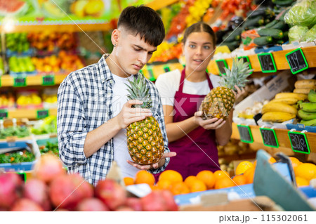 Friendly young saleswoman helps a guy buyer choose a pineapple Friendly young saleswoman helps a guy buyer choose a pineapple 115302061