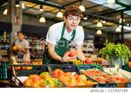 European male seller in apron takes tomatoes from window 115302190
