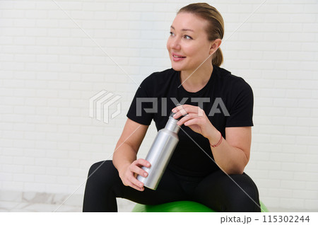 Young sporty woman resting with water bottle after home workout session Young sporty woman resting with water bottle after home workout session 115302244