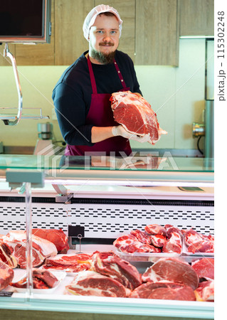 Friendly bearded butcher offering fresh beef cut 115302248
