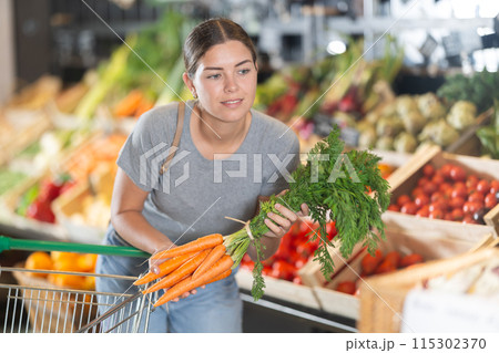 In vegetable department of bio supermarket, female customer took bunch of carrots from window 115302370