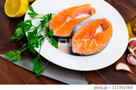 Raw salmon steaks, parsley, garlic and lemon on plate 115302568