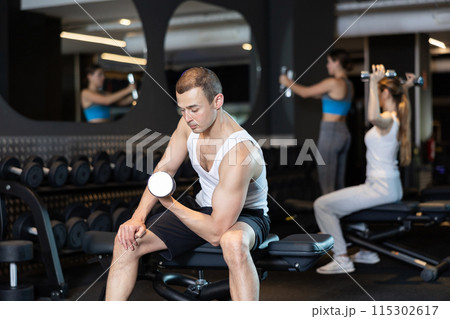 Determined young man working out with dumbbell in sports hall Determined young man working out with dumbbell in sports hall 115302617