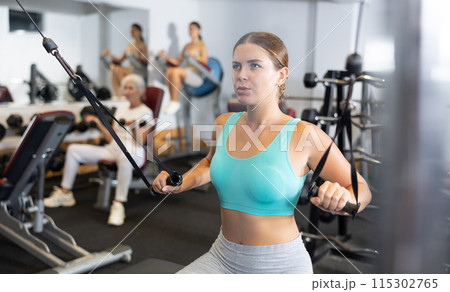 Athletic woman working on special machine with ropes to develop arm muscles 115302765