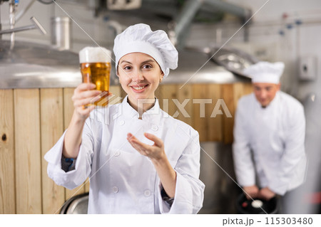 Successful female brewmaster holding glass of foamy ale Successful female brewmaster holding glass of foamy ale 115303480