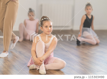 During lesson at ballet studio, girl sits on floor and thinks, dreams. During lesson at ballet studio, girl sits on floor and thinks, dreams. 115303490