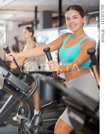 Portrait of sporty woman doing cardio workout on elliptical cross trainer at fitness center 115303700